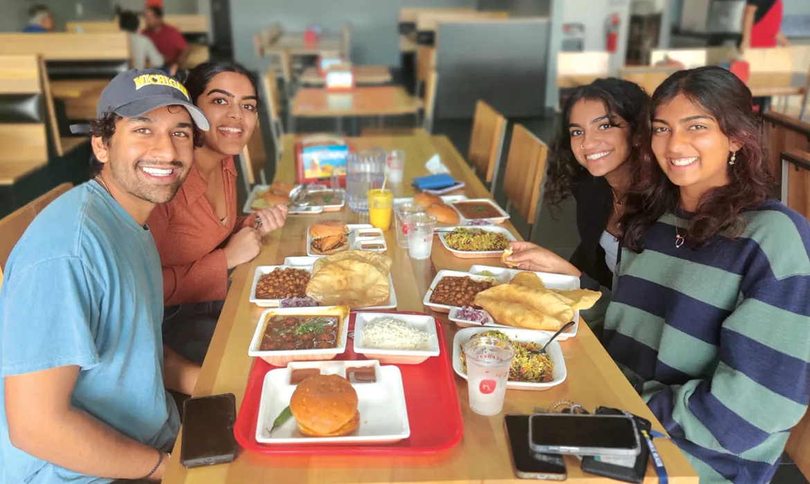 Group of young adults enjoying a meal together at a restaurant table filled with Indian street food dishes at Neehee's