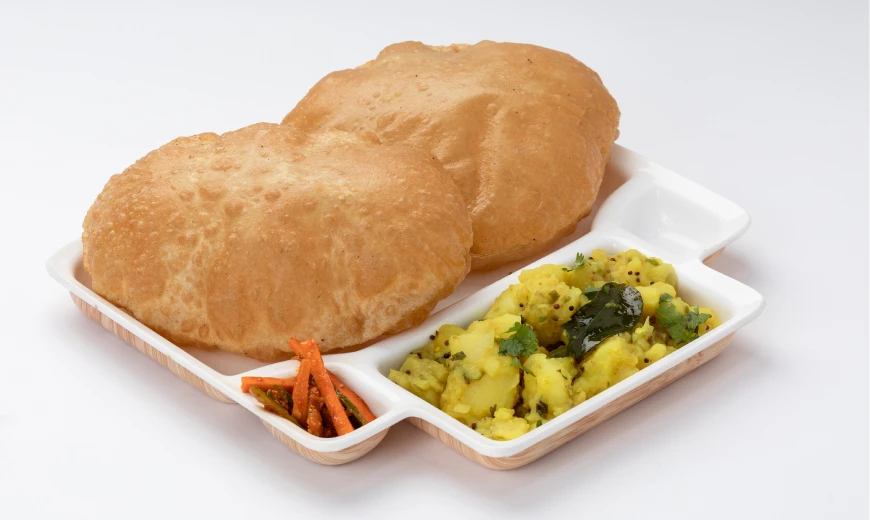 Neehee's Puri Bhaji. Two pieces of puffed fried bread (poori) served with spiced potato curry and a small portion of pickled vegetables on a white tray.