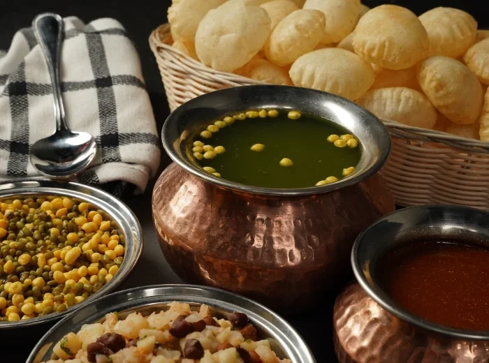 Traditional Indian pani puri with crispy puffed puris, served with spicy green chutney, tangy tamarind sauce, and bowls of spiced chickpeas and potato filling in a copper and steel setup.