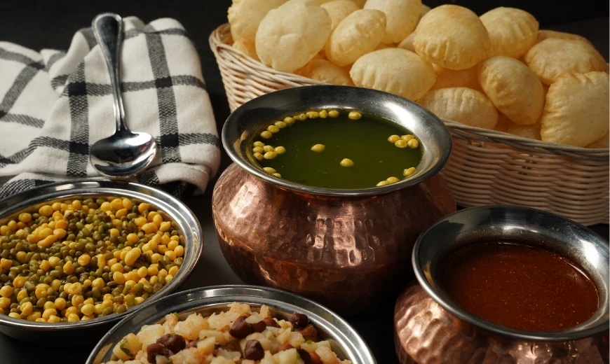 Traditional Indian pani puri with crispy puffed puris, served with spicy green chutney, tangy tamarind sauce, and bowls of spiced chickpeas and potato filling in a copper and steel setup.