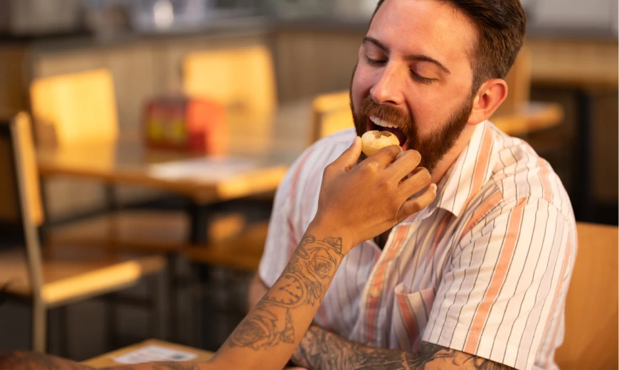 Man enjoying a bite of food being fed by a companion at a restaurant, creating a warm and playful dining moment at Neehee's Restaurant